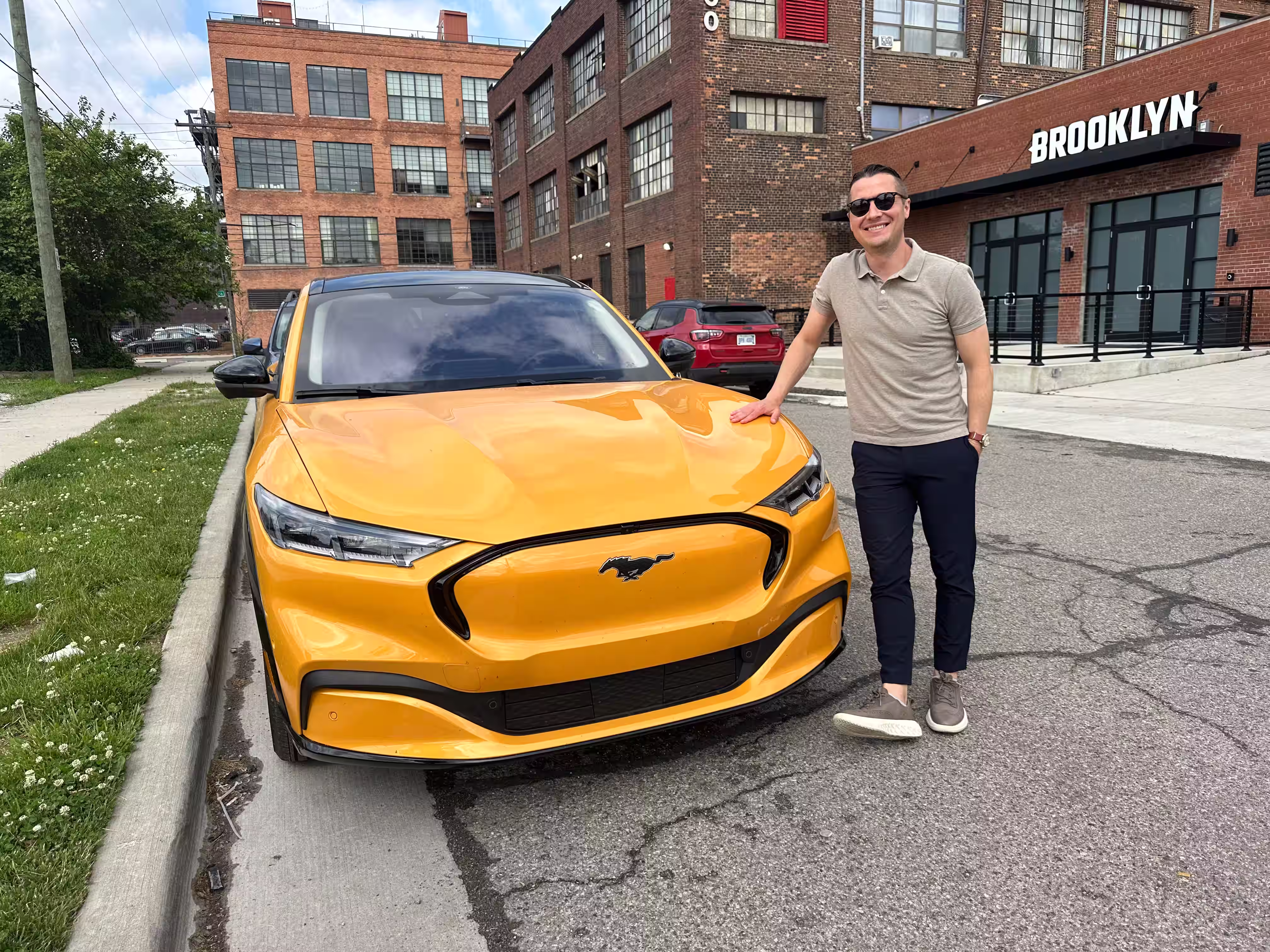Devon smiling while standing next to a yellow Ford Mach-E electric vehicle.